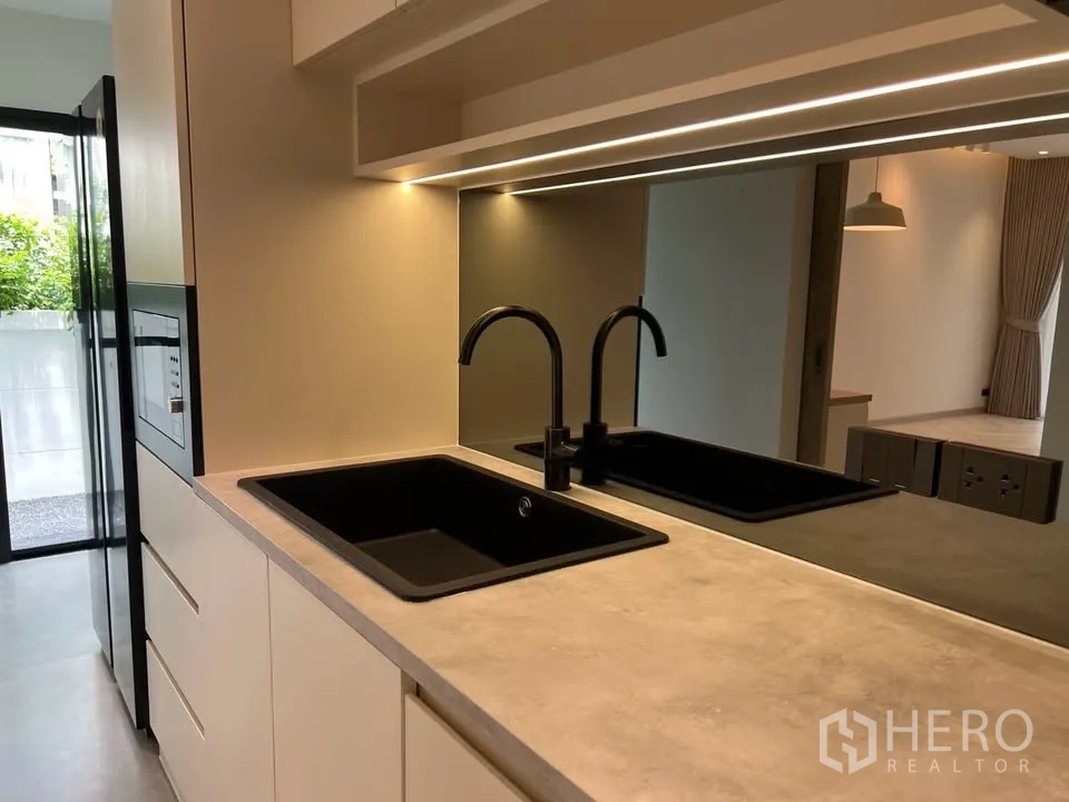 Townhouse for rent in Prawet, Bangkok - Close-up of dual black sinks and lit backsplash in kitchen.
