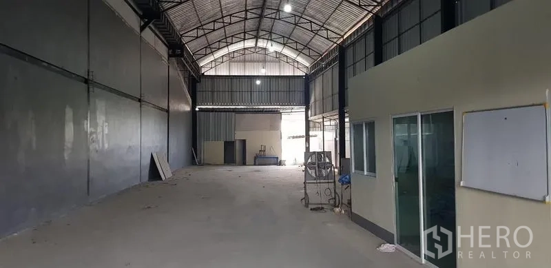 货栈 出租在Bang Phli, Samut Prakan - 宽敞仓库大厅，高挑钢结构屋顶与混凝土地面，侧边为办公室隔间。