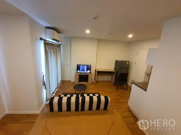 Condominium for sale in Chatuchak, Bangkok - Cozy Chatuchak condo living area with striped sofa, TV, work desk and fridge on wood floors.