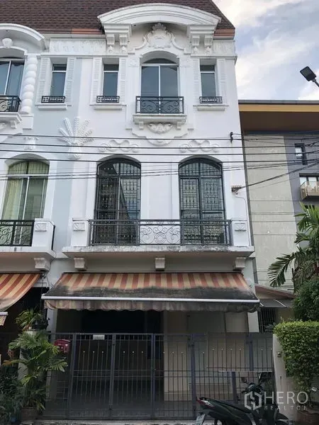 ทาวน์เฮาส์ ให้เช่าในWang Thonglang, Bangkok - ด้านหน้าทาวน์เฮ้าส์ 3 ชั้นสไตล์ยุโรป พร้อมระเบียงเหล็กดัด กันสาดลายทาง และที่จอดรถมีรั้ว ในย่านวังทองหลาง กรุงเทพฯ