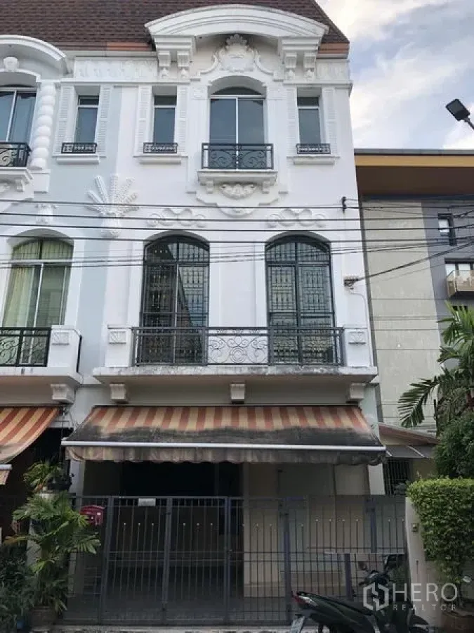 ทาวน์เฮาส์ ให้เช่าในWang Thonglang, Bangkok - ด้านหน้าทาวน์เฮ้าส์ 3 ชั้นสไตล์ยุโรป พร้อมระเบียงเหล็กดัด กันสาดลายทาง และที่จอดรถมีรั้ว ในย่านวังทองหลาง กรุงเทพฯ