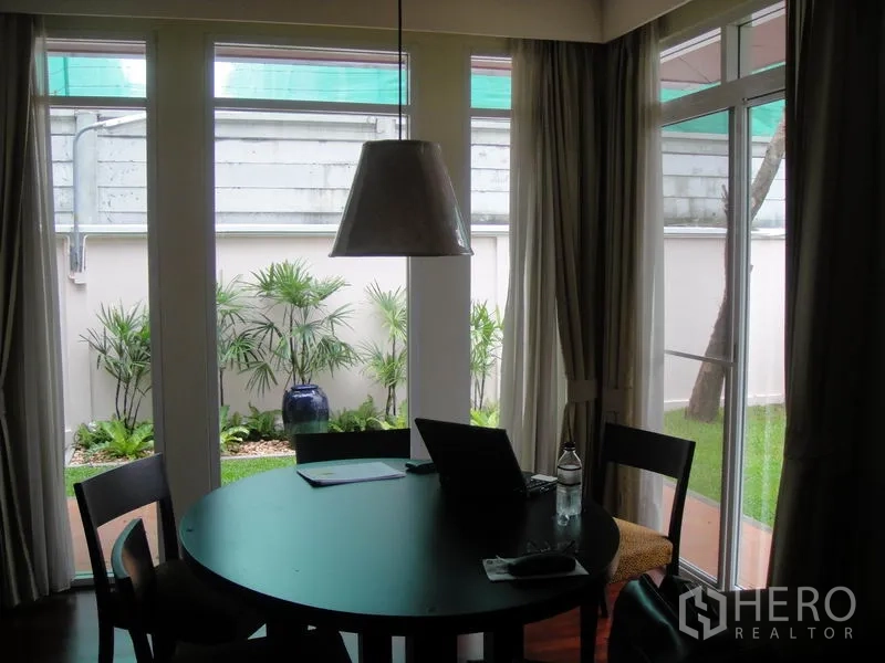 Detached House for rent in Wang Thonglang, Bangkok - Dining nook with round table, pendant light and garden views through glass doors.