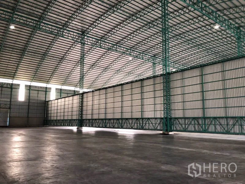 Warehouse for rent in Sai Noi, Nonthaburi - Long partition wall beneath arched truss roof and smooth concrete floor.