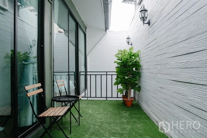 Townhouse for rent in Watthana, Bangkok - Private balcony with artificial grass, small bistro table set and large sliding glass doors.