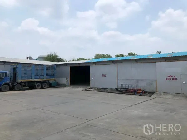 货栈 出租在Mueang Pathum Thani, Pathum Thani - 仓库外立面设有多处装卸门，宽大车道上停着集装箱卡车。