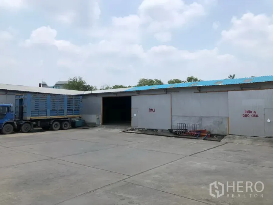 货栈 出租在Mueang Pathum Thani, Pathum Thani - 仓库外立面设有多处装卸门，宽大车道上停着集装箱卡车。