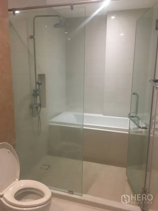 公寓 出租在Khlong Toei, Bangkok - 浴室设玻璃淋浴间、浴缸与白色瓷砖装饰。