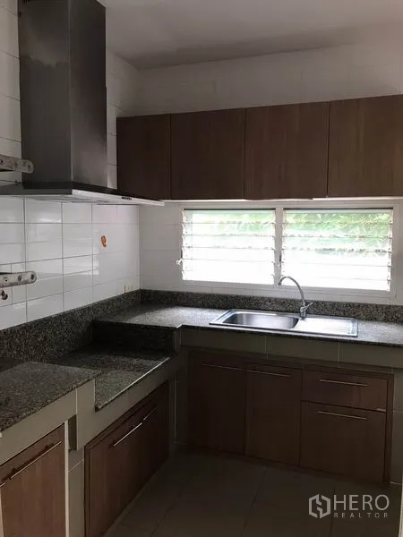Detached House for rent in Khlong Sam Wa, Bangkok - Fitted kitchen with granite countertops, sink under window and wood cabinetry.