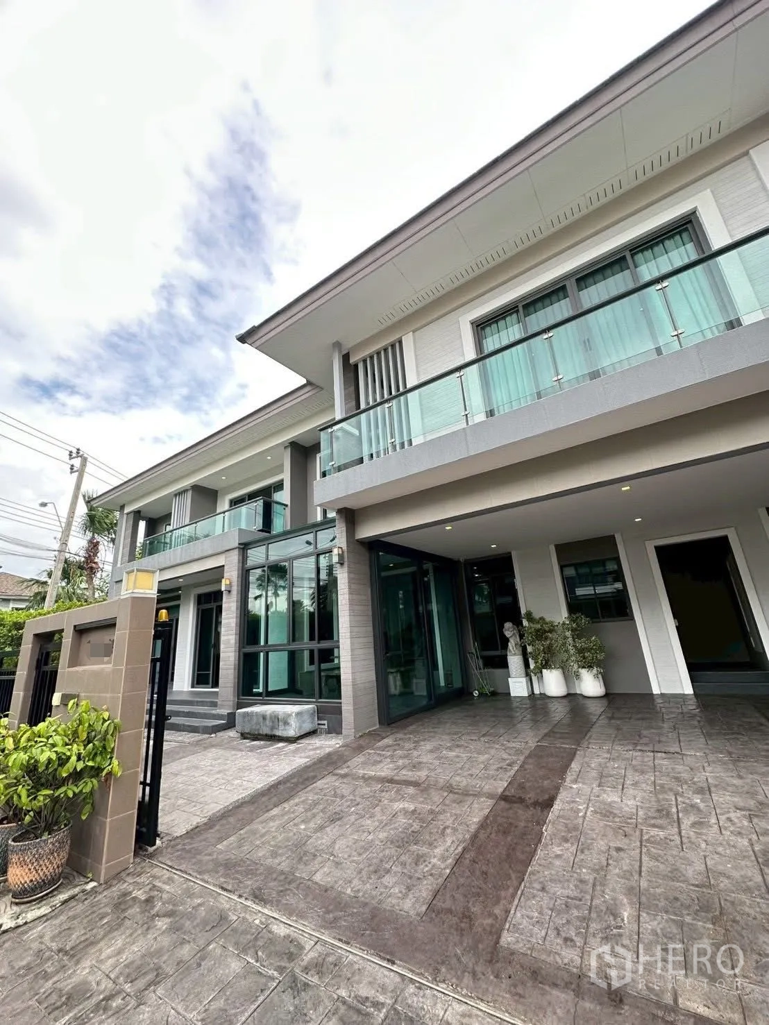 Detached House for sale in Bang Lamung, Chon Buri - Front façade angle showing gate, wide driveway, floor-to-ceiling windows and a sleek balcony.