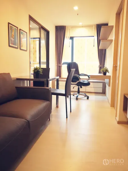 公寓 出租在Khlong Toei, Bangkok - 明亮客厅，配沙发、玻璃餐桌、窗边书桌及通往卧室的玻璃推门。