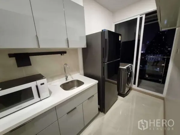 公寓 出租 - 现代一字型厨房，灰色柜体，冰箱与洗衣机临近阳台夜景。