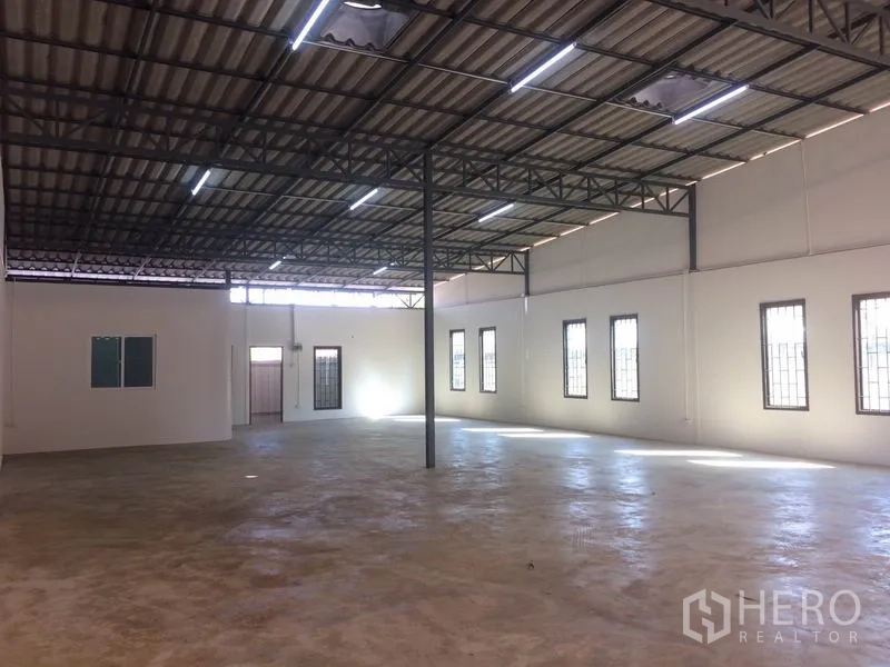 Warehouse for rent in Lam Luk Ka, Pathum Thani - Open-plan warehouse hall with steel trusses, bright side windows and skylight panels, and polished concrete flooring.