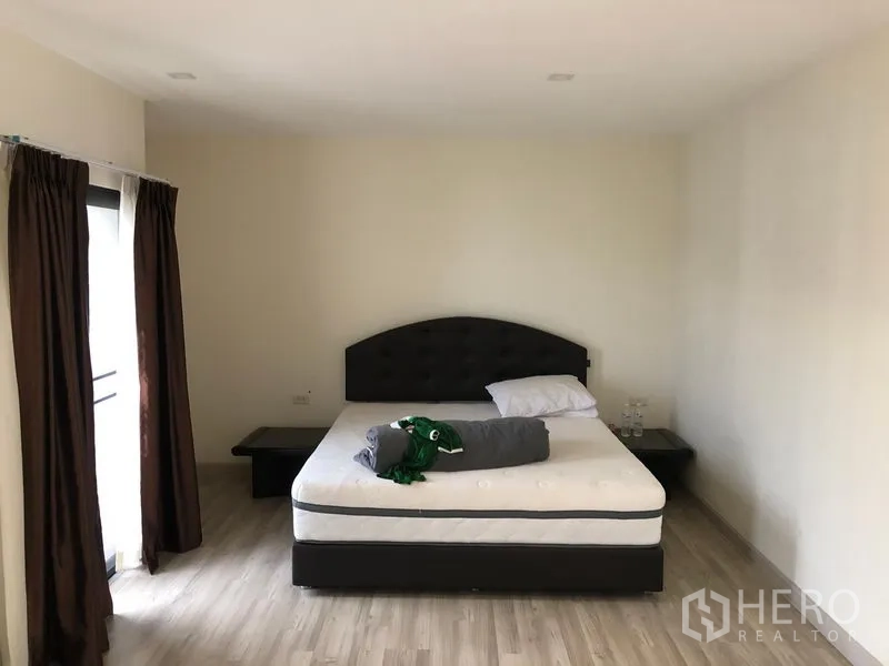 Townhouse for rent or sale in Saphan Sung, Bangkok - Bedroom with double bed, nightstands and dark curtains beside a balcony door.
