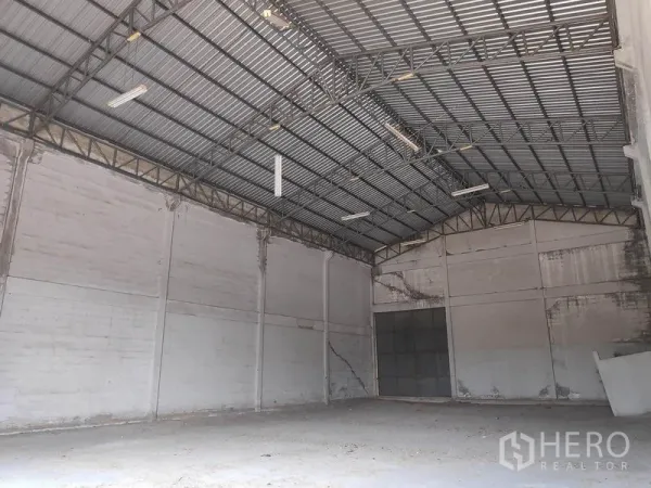 工厂 出租在Sai Noi, Nonthaburi - 空置工厂内部，高挑钢桁架屋顶、混凝土地面与大型滑门。