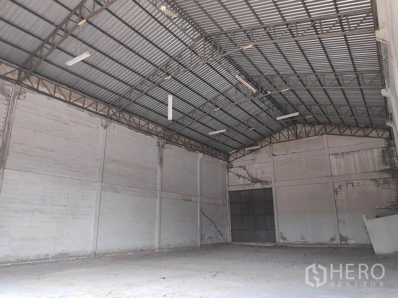 工厂 出租在Sai Noi, Nonthaburi - 空置工厂内部，高挑钢桁架屋顶、混凝土地面与大型滑门。