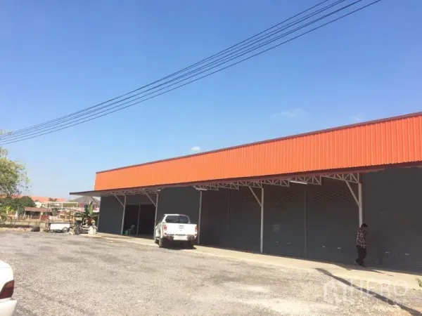 货栈 出租在Pathum Thani - 仓库外观，橙色山墙，多个卷帘门，前方有宽阔装卸与停车场地，位于兰鲁甲。