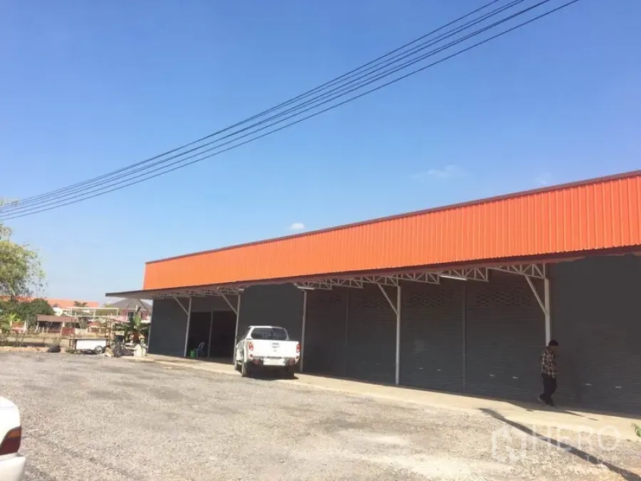 货栈 出租在Pathum Thani - 仓库外观，橙色山墙，多个卷帘门，前方有宽阔装卸与停车场地，位于兰鲁甲。