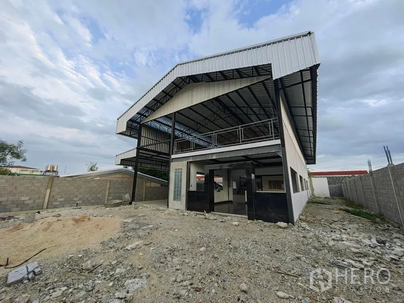 Factory for rent or sale in Mueang Samut Prakan, Samut Prakan - Front exterior of a two-storey factory with cantilevered metal roof and gated entrance.