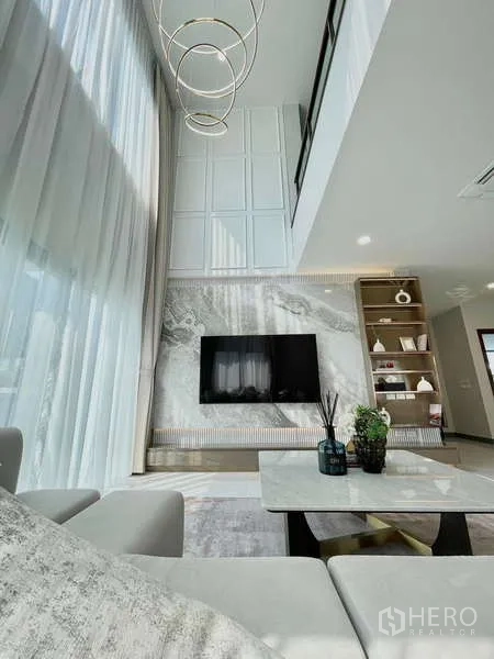 Detached House for rent in Bang Phli, Samut Prakan - Double-height living room featuring a marble TV wall, statement chandelier and tall curtains.
