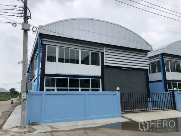 工厂 出租或出售在Bang Bua Thong, Nonthaburi - 现代化工厂外观，浅蓝围墙，大型卷帘门与二层办公室窗户。