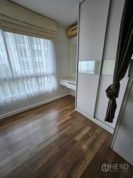 Condominium for sale in Watthana, Bangkok - Bedroom corner with large wardrobe, vanity, and window with sheer curtains.