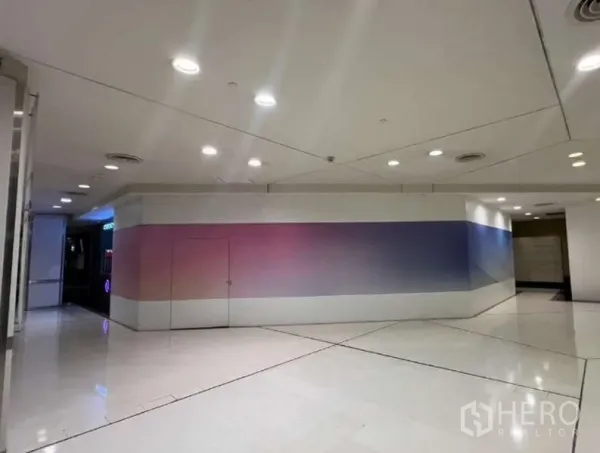 零售空间 出租 - 明亮购物通道旁的封闭店面，聚光灯照明与宽阔门面，适合醒目招牌与高曝光。