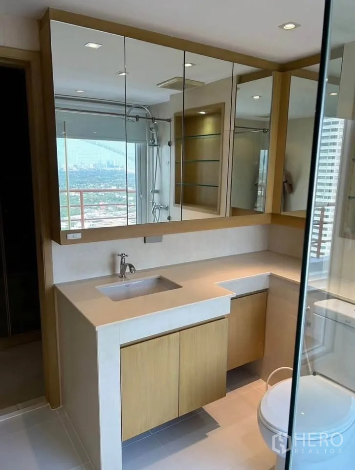 Condominium for rent or sale in Yan Nawa, Bangkok - Bathroom vanity with mirrored cabinets, under-counter storage and city view reflection.