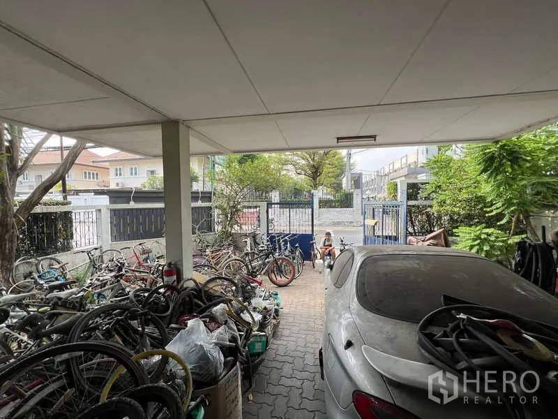 独立式住宅 出售在Suan Luang, Bangkok - 前院带有顶棚车库与车道，通向街边的金属大门。
