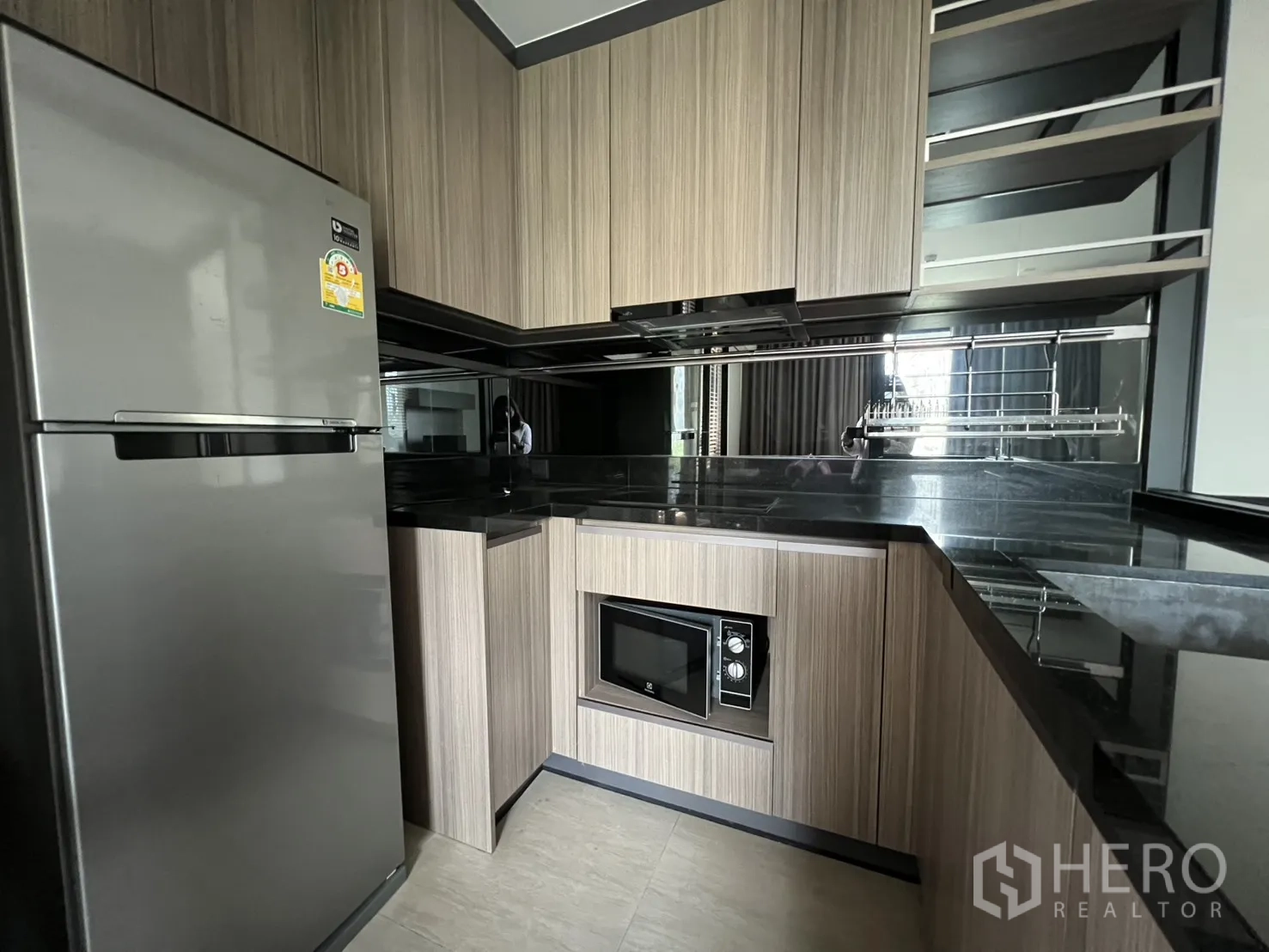 Condominium for rent in Watthana, Bangkok - Modern L-shaped kitchen with refrigerator, microwave, ample cabinets, and glossy black counters.