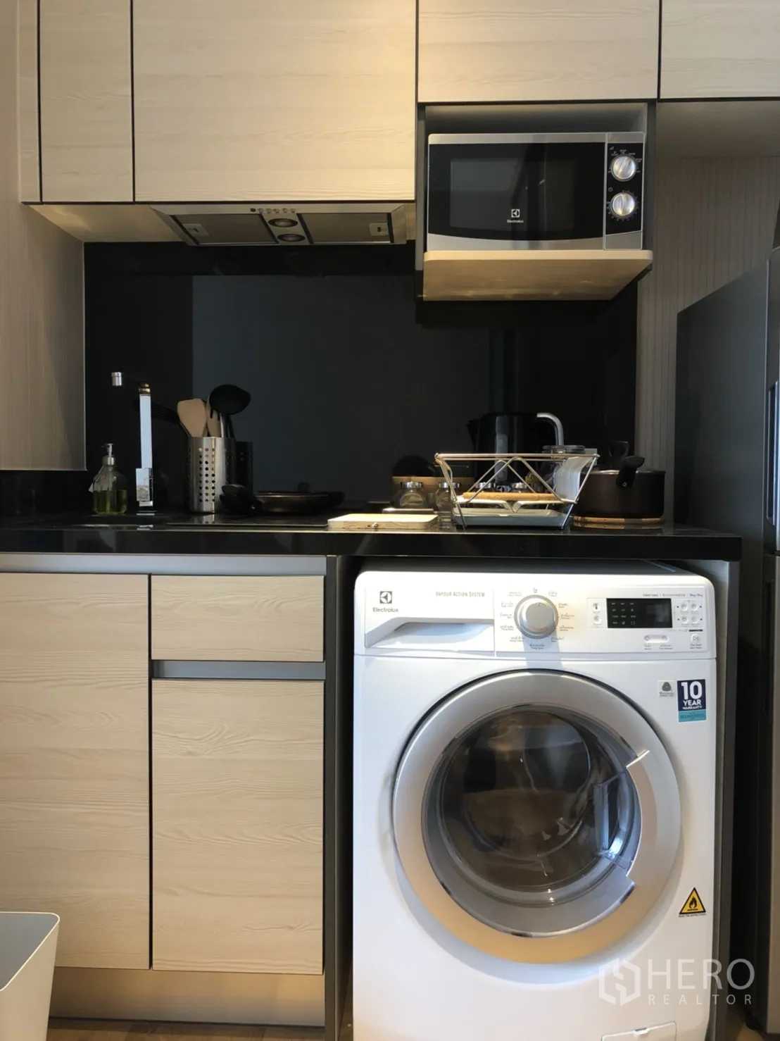 Condominium for rent in Khlong Toei, Bangkok - Compact kitchenette with upper cabinets, cooktop, microwave and front-load washing machine.