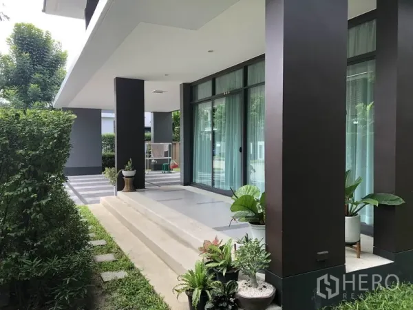 Detached House for rent or sale in Bang Kapi, Bangkok - Shaded front terrace with steps, tall columns and sliding glass doors surrounded by greenery.