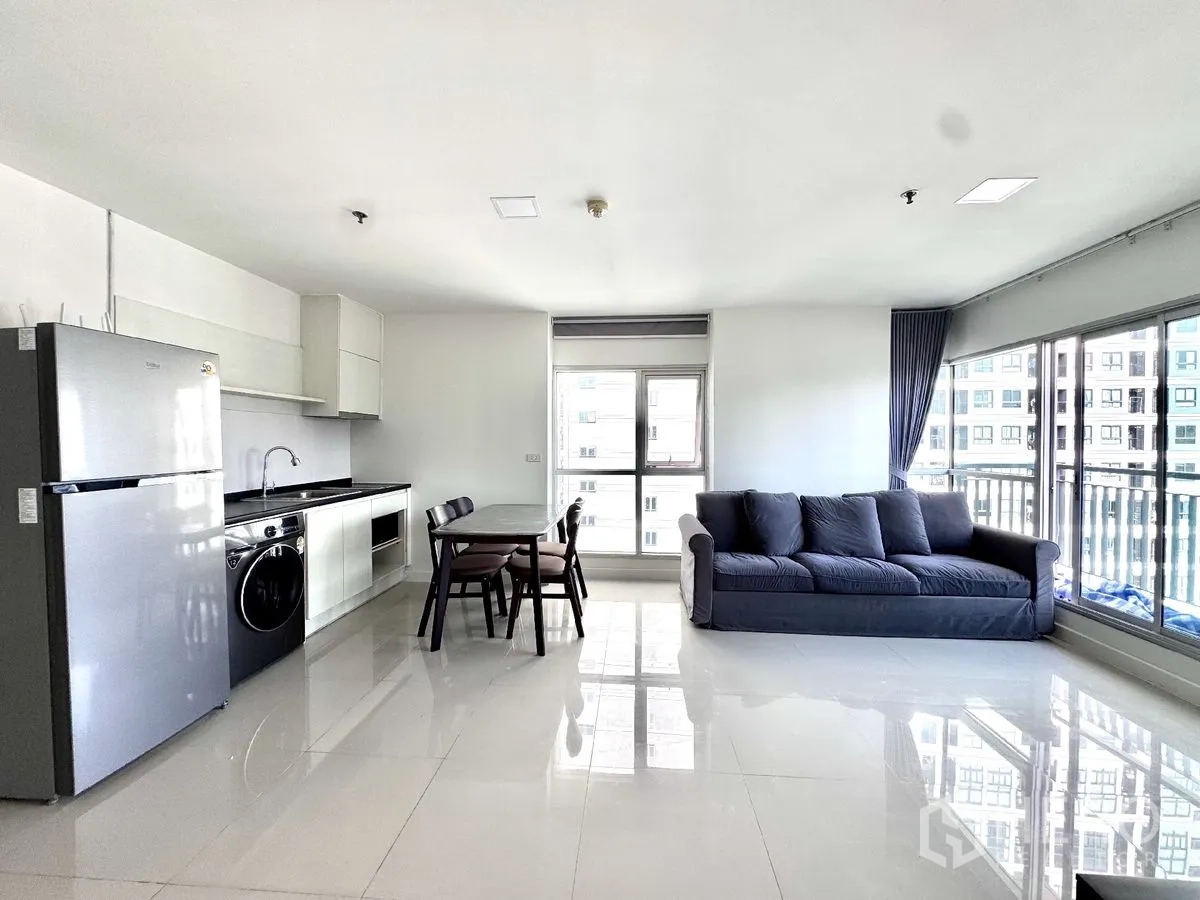Condominium for rent in Huai Khwang, Bangkok - Open-plan living area with kitchenette, refrigerator, washing machine, dining table, and sofa.