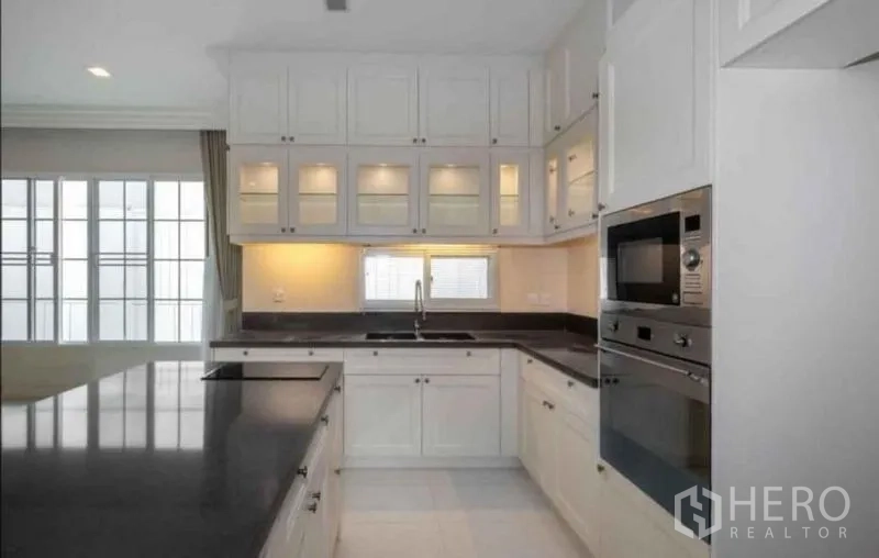 Detached House for rent or sale in Bang Phli, Samut Prakan - U-shaped Western kitchen with built-in oven and microwave, glass-front cabinets and task lighting.