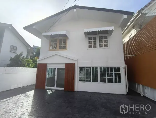 Detached House for rent in Bang Na, Bangkok - Front exterior of a two-storey white detached house in Bang Na with sliding glass doors, window awnings and a large paved driveway.