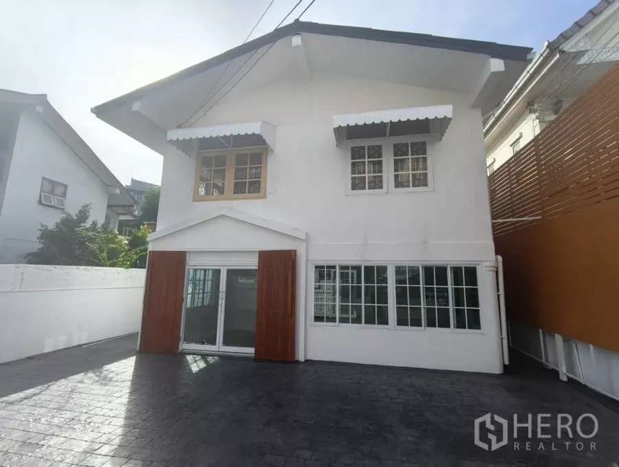 บ้าน ให้เช่าในBang Na, Bangkok - ด้านหน้าบ้านเดี่ยวสองชั้นสีขาวในย่านบางนา ประตูบานเลื่อน กระจก กันสาด และลานจอดรถปูพื้นกว้าง