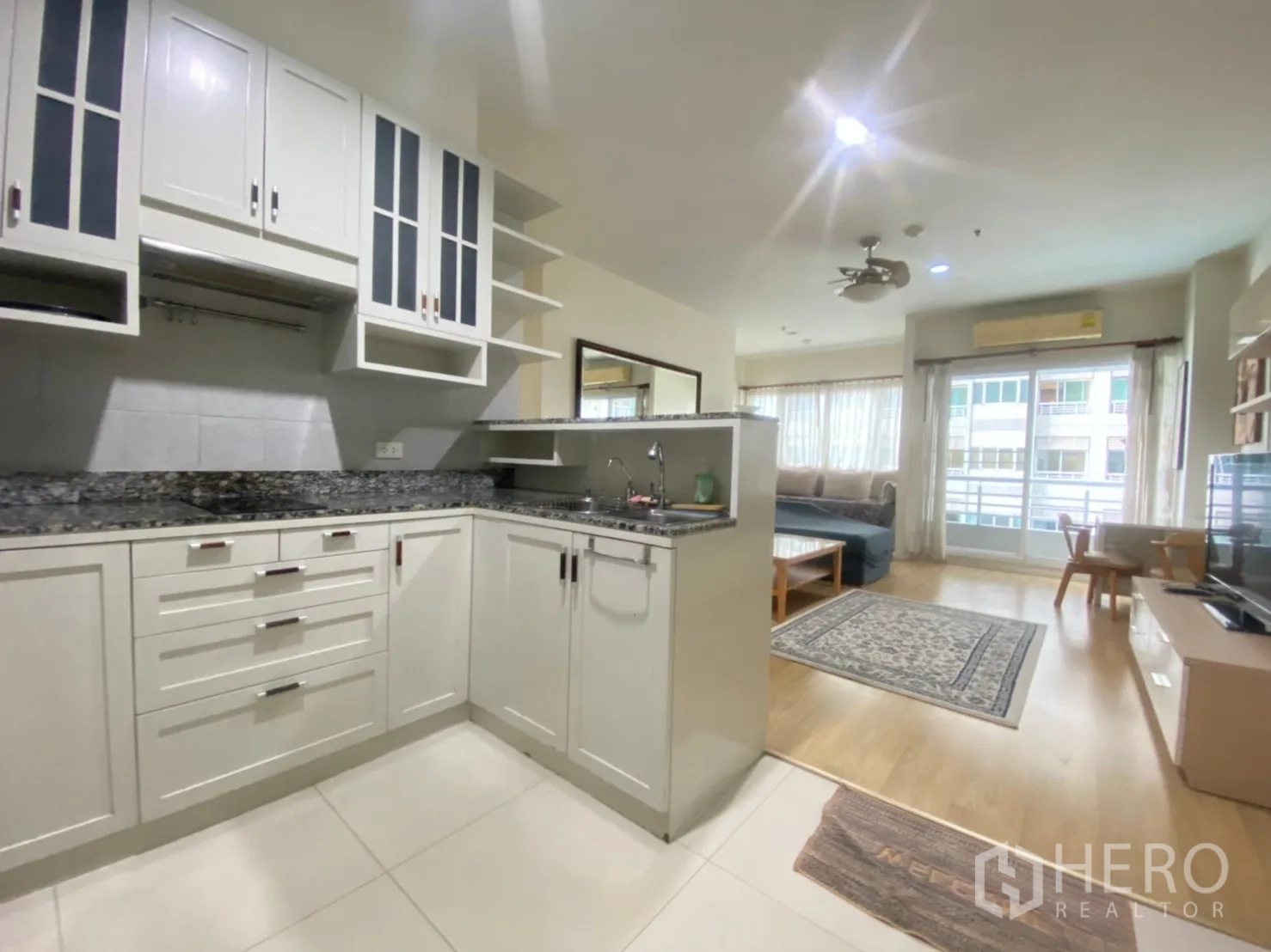 คอนโด ให้เช่าในBang Kapi, Bangkok - ครัวแบบเปิดตู้สีขาวเคาน์เตอร์หินแกรนิตเชื่อมต่อห้องนั่งเล่นสว่างพร้อมระเบียง