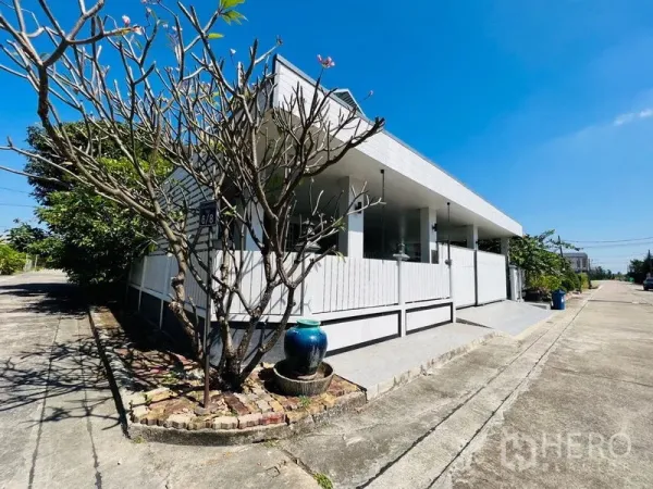 บ้าน ขายในLat Krabang, Bangkok - มุมภายนอกบ้านเดี่ยวสีขาวพร้อมรั้วและต้นไม้ริมถนนแดดจัด