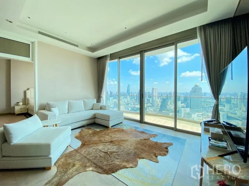 Condominium for rent in Khlong San, Bangkok - Living area with expansive floor‑to‑ceiling windows, white sectional sofa, and dramatic city panorama.