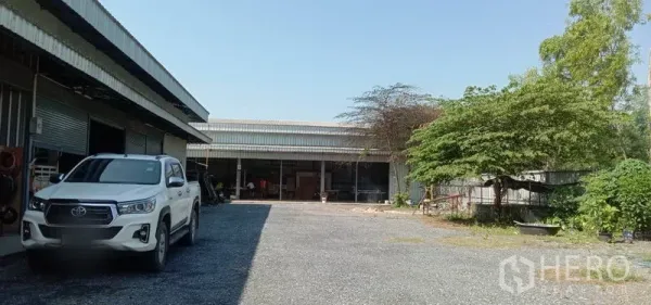 คลังสินค้า ให้เช่าในKhlong Sam Wa, Bangkok - ลานกว้างปูหินกรวดระหว่างอาคารโกดัง มีเงาต้นไม้และจุดขนถ่ายสินค้า