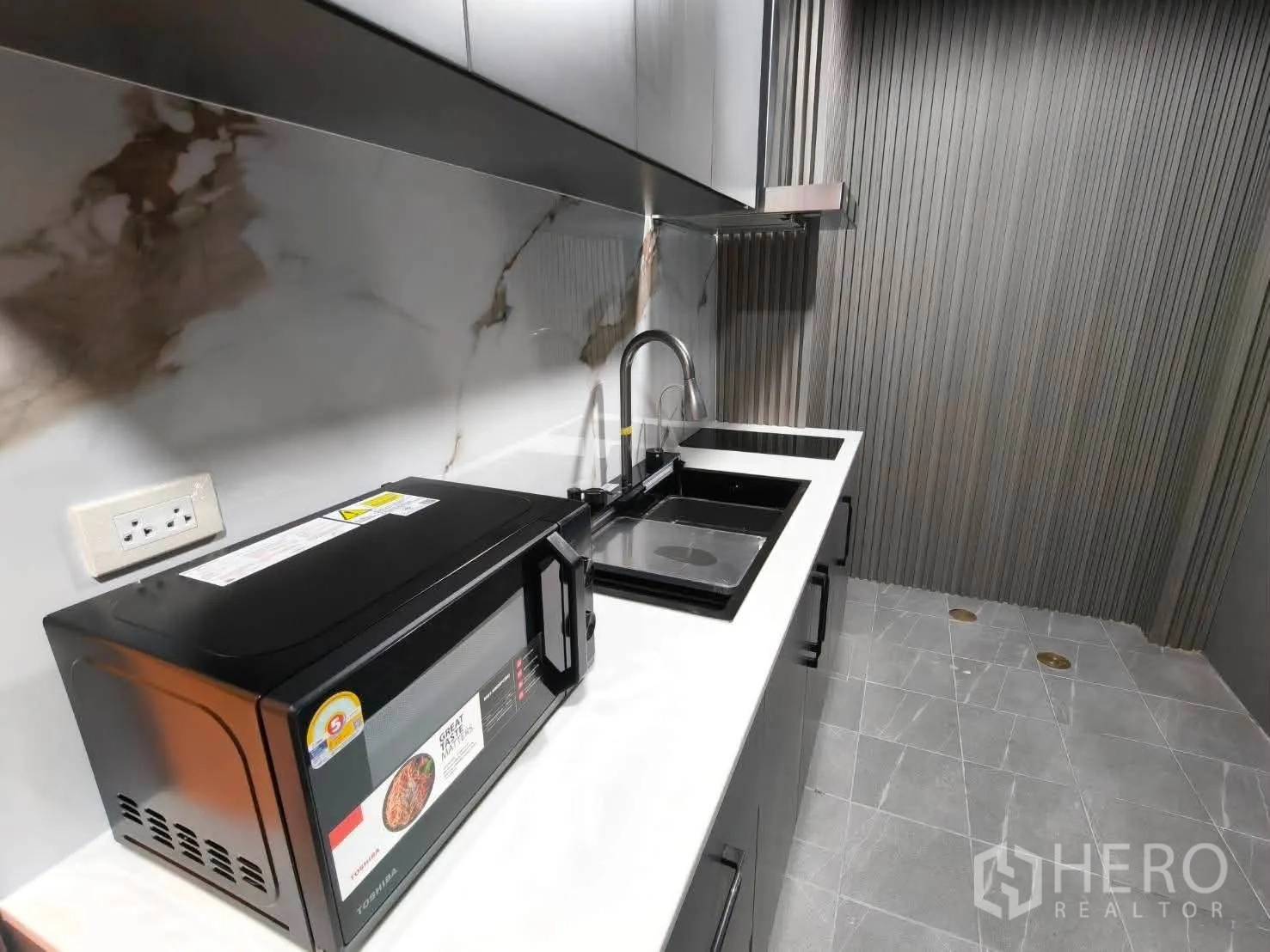 Townhouse for rent in Bang Phli, Samut Prakan - Modern kitchenette with marble-look backsplash, microwave, sink and electric cooktop.