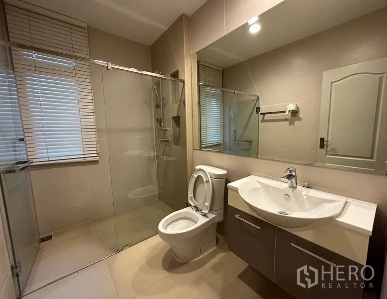 Detached House for rent or sale in Khan Na Yao, Bangkok - Bright bathroom with glass shower, toilet, wide mirror and modern vanity.