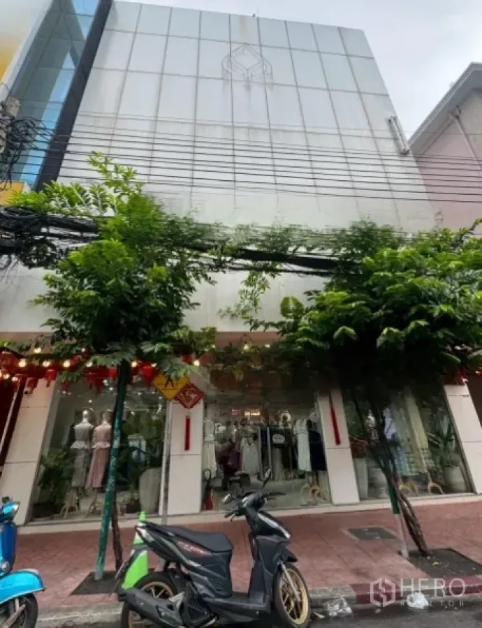 Shophouse for rent in Samphanthawong, Bangkok - Modern multi-storey shophouse facade with full-height glass storefront and trees on the sidewalk.