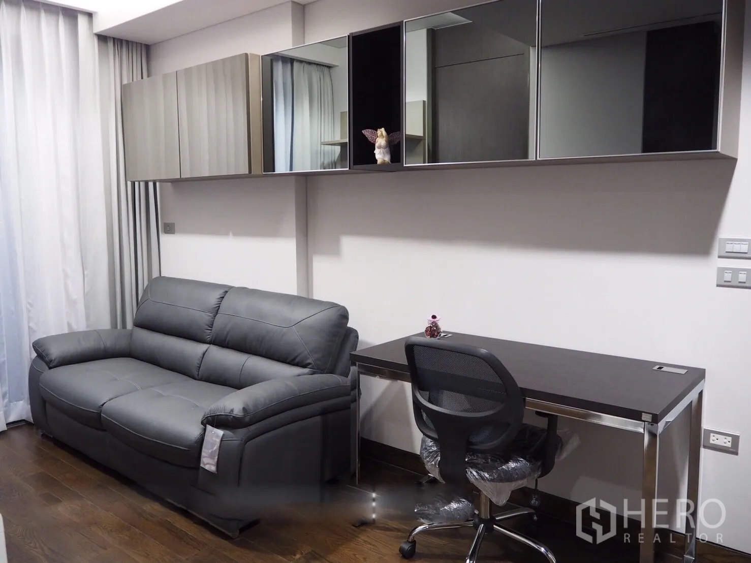 Condominium for rent in Khlong Toei, Bangkok - Modern living area with gray leather sofa, work desk and wall cabinets on wood floors.