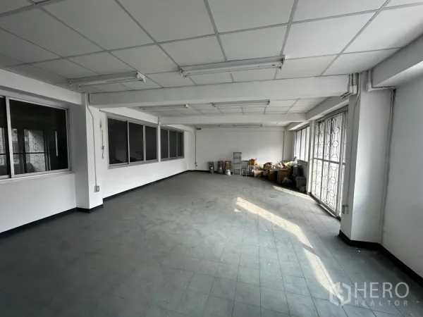 Factory for rent or sale in Khlong Luang, Pathum Thani - Large office or storage room with windows, fluorescent lighting and a metal security gate.