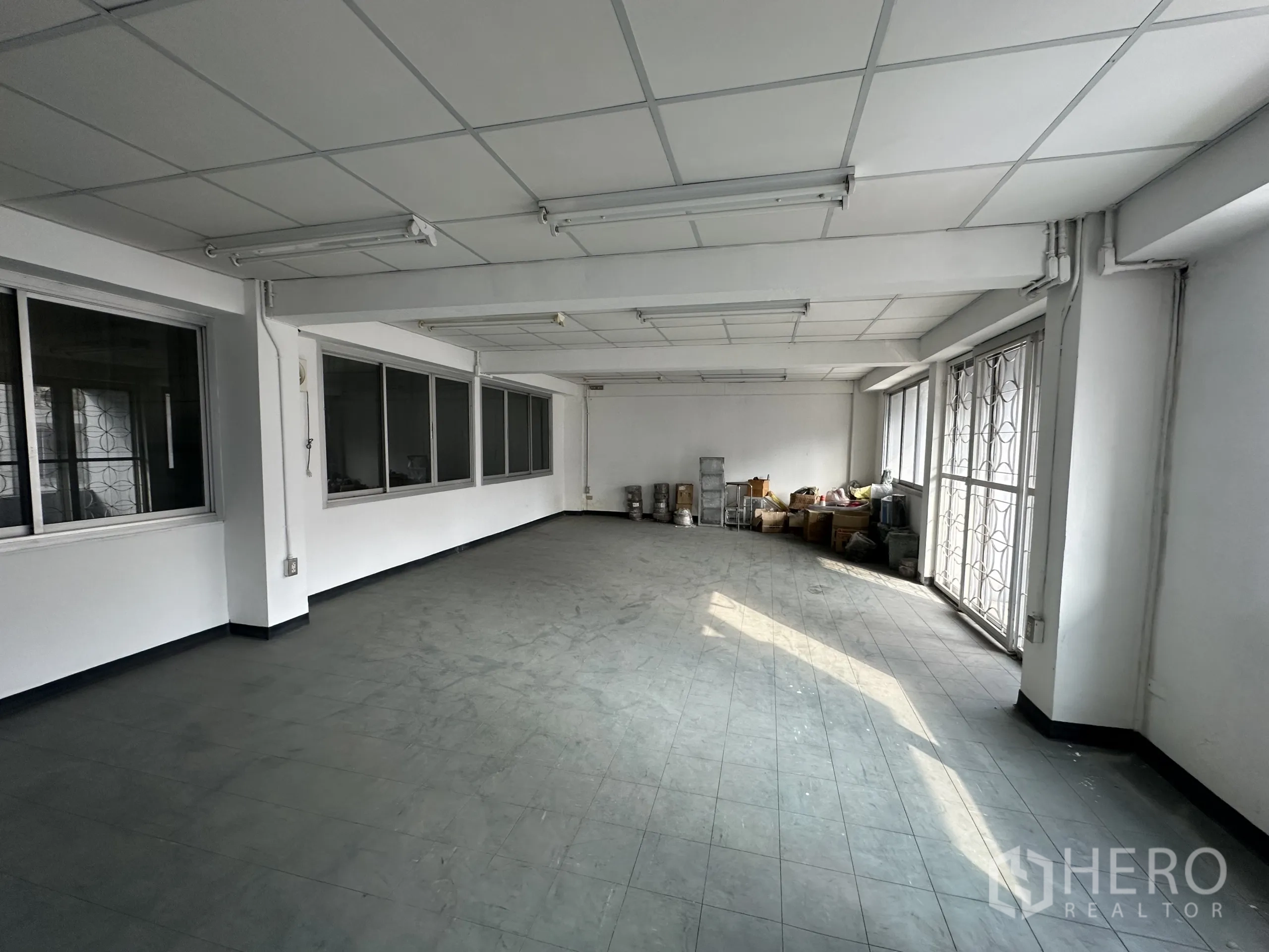 Factory for rent or sale in Khlong Luang, Pathum Thani - Large office or storage room with windows, fluorescent lighting and a metal security gate.