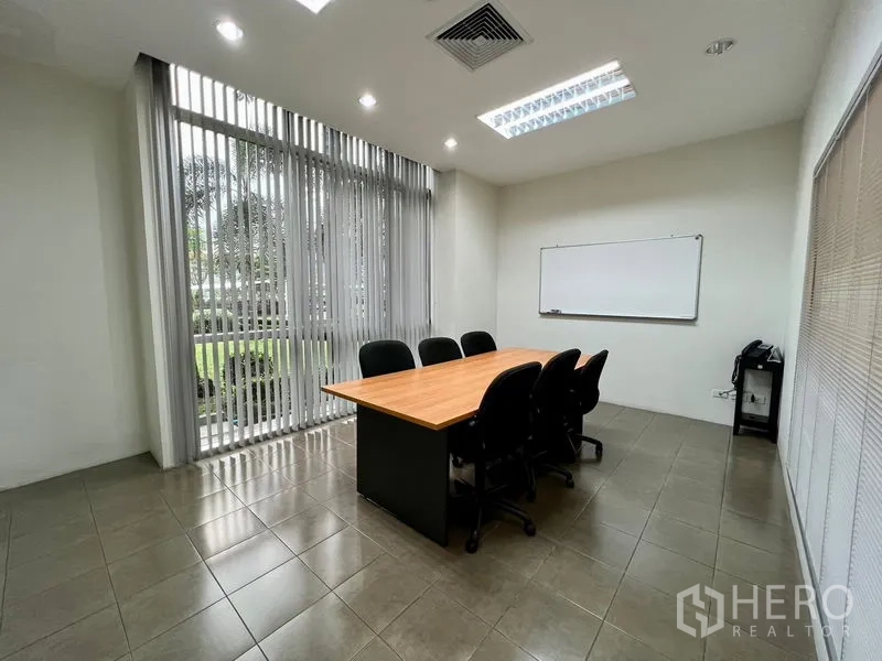 Office Space for rent in Bueng Kum, Bangkok - Glass-walled meeting room with a long table, seating for eight, whiteboard, and vertical blinds overlooking greenery.