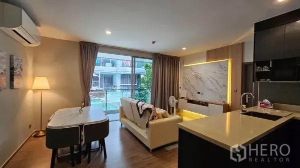 คอนโด ให้เช่า - ห้องนั่งเล่นแบบเปิดโล่งพร้อมเคาน์เตอร์ไอแลนด์ ผนังลายหินอ่อน และระเบียงมองเห็นสระว่ายน้ำคอร์ตยาร์ดในคอนโดสมัยใหม่