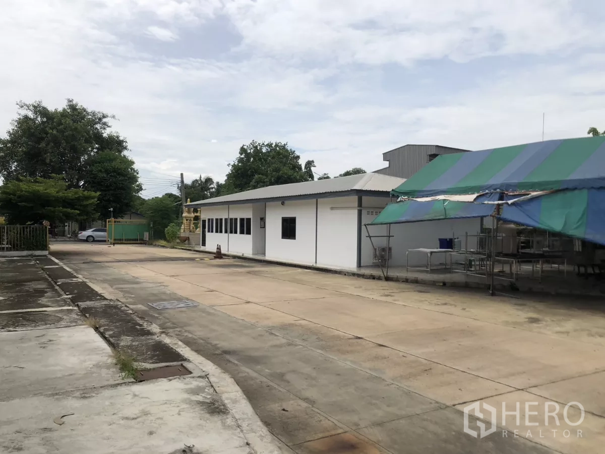 Factory for rent in Mueang Samut Prakan, Samut Prakan - Side of the office building with tented work area and wide concrete yard