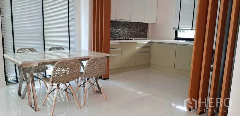 Detached House for rent in Bang Phli, Samut Prakan - Open dining area and L-shaped kitchen with white cabinets, mosaic backsplash and a marble-top table.
