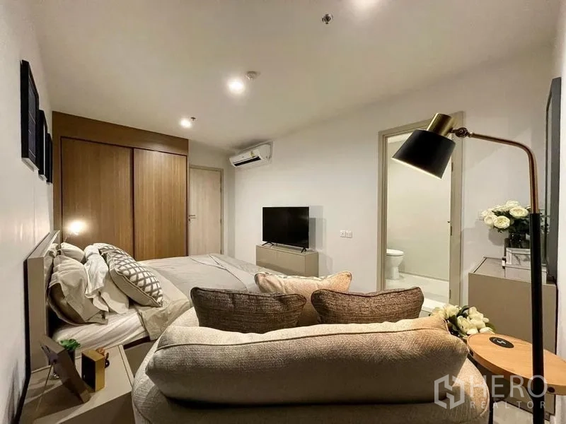 Condominium for rent in Pathum Wan, Bangkok - Primary bedroom angle showing loveseat, TV console, air conditioner and door to ensuite.